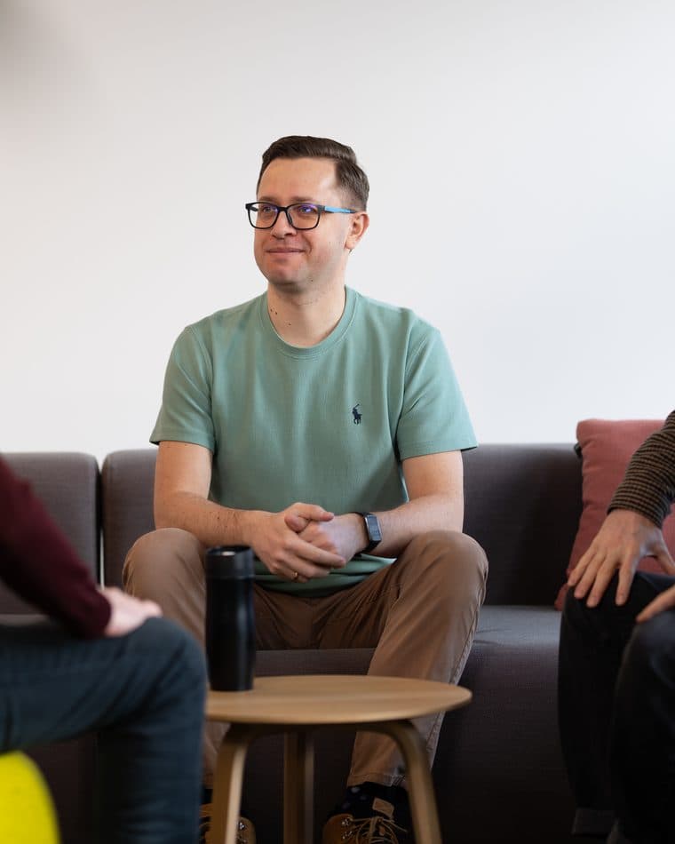 Platzhalter-Teamfoto (Stockfoto): ein Mann in hellgrünem T-Shirt sitzt lächelnd auf einem Sofa im Büro — echter Name und Foto folgen vor Live-Gang (siehe AGENTS.md Abschnitt 7).